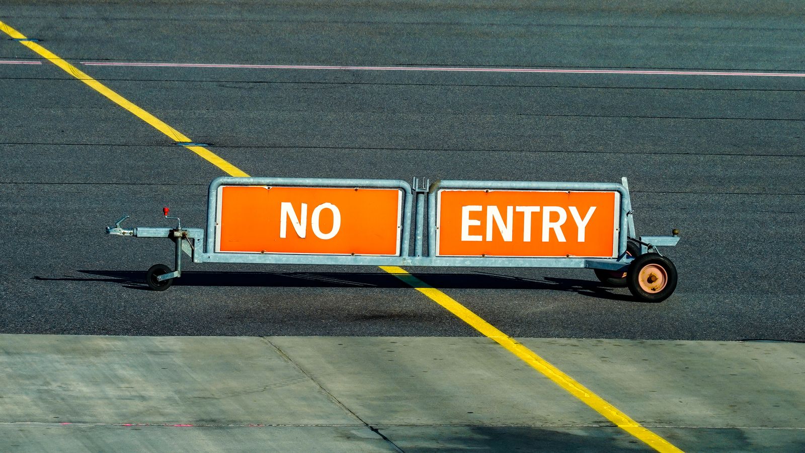 A warning sign indicating no entry on an airport taxiway with a bold yellow line.