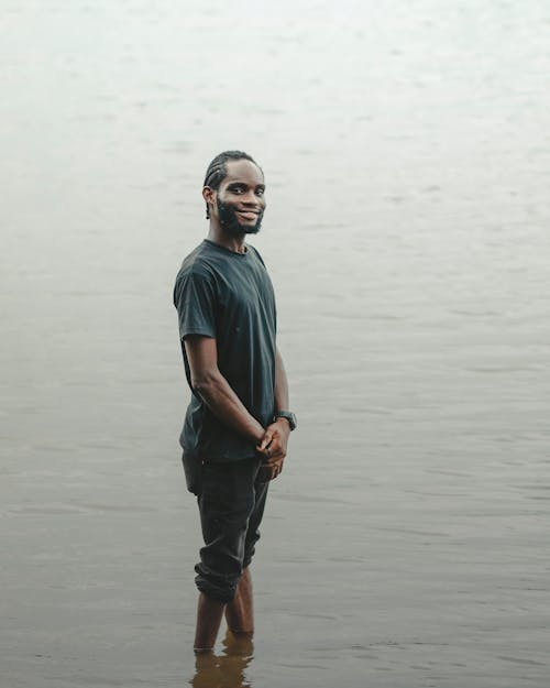 Man in Gray T-Shirt and Rolled Up Black Pants Standing in Water