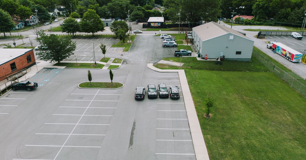 Drone shot of a parking lot in Chattanooga with cars and buildings, surrounded by lush greenery.