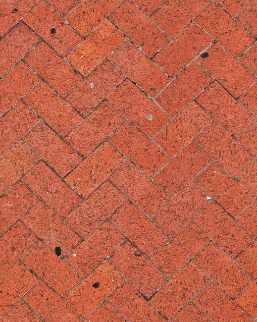 Close-up of a textured red brick pavement in a classic herringbone pattern.