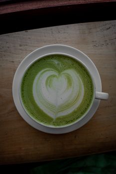Photo by Connor Scott McManus A top view of a matcha latte with heart shaped froth art in a white cup on a wooden table.