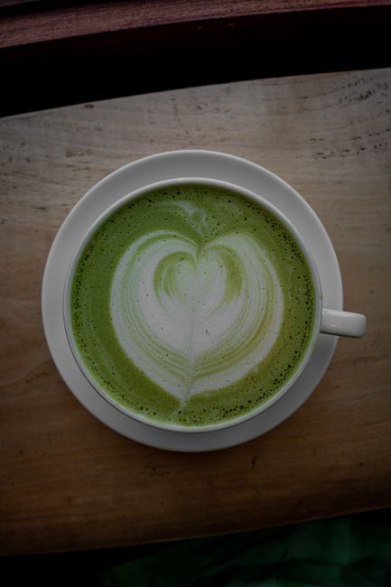 Photo by Connor Scott McManus A top view of a matcha latte with heart shaped froth art in a white cup on a wooden table.