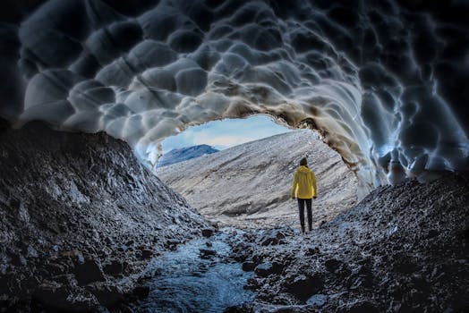 A person in a yellow jacket stands at the entrance of an ice cave in Iceland, showcasing nature's raw beauty.