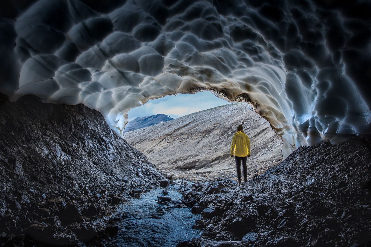 a person in a yellow jacket stands at the entrance of an ice cave in i