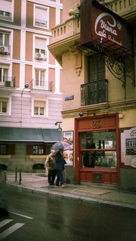 Charming city street scene with people under umbrellas by a cafe on a rainy day.