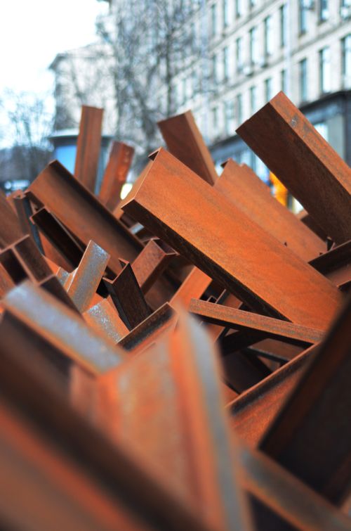 Free A visually striking close-up of stacked rusty iron beams in an urban setting, reflecting industrial decay. Stock Photo