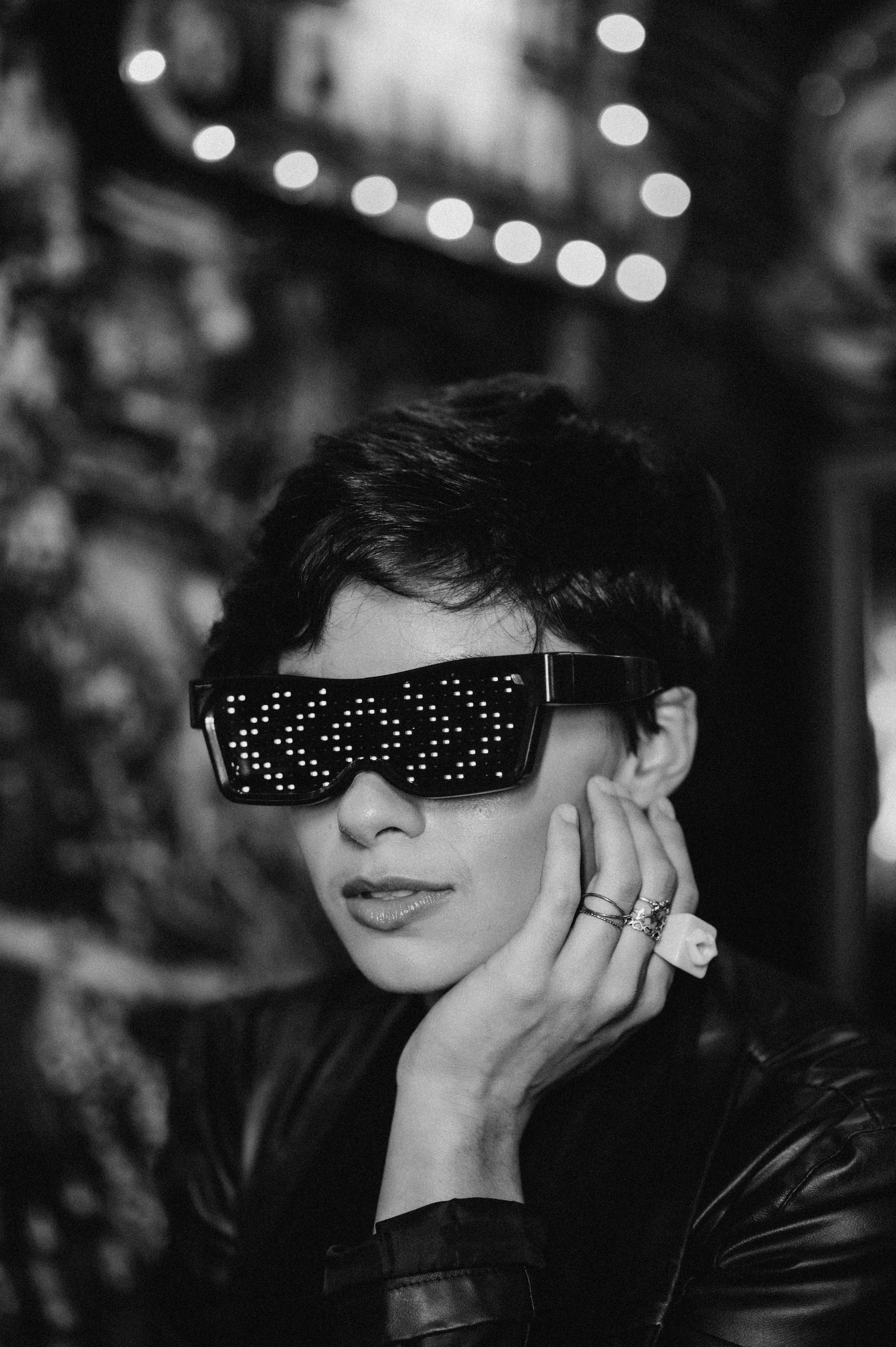 Black and white portrait of a woman with short hair wearing sunglasses, hand on cheek.