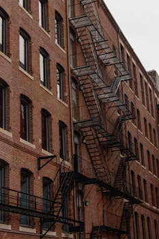 Brick building with metal fire escape stairs in urban setting, vertical view.