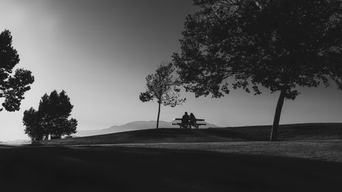 Free Silhouette of a couple sitting on a park bench surrounded by trees at twilight. Stock Photo
