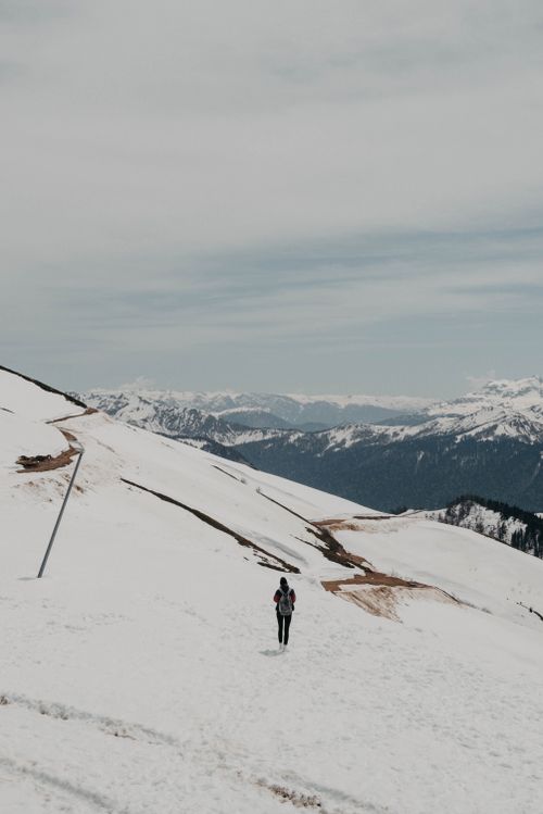 Free A lone hiker traversing a vast snow-covered mountain range under a cloudy winter sky. Stock Photo
