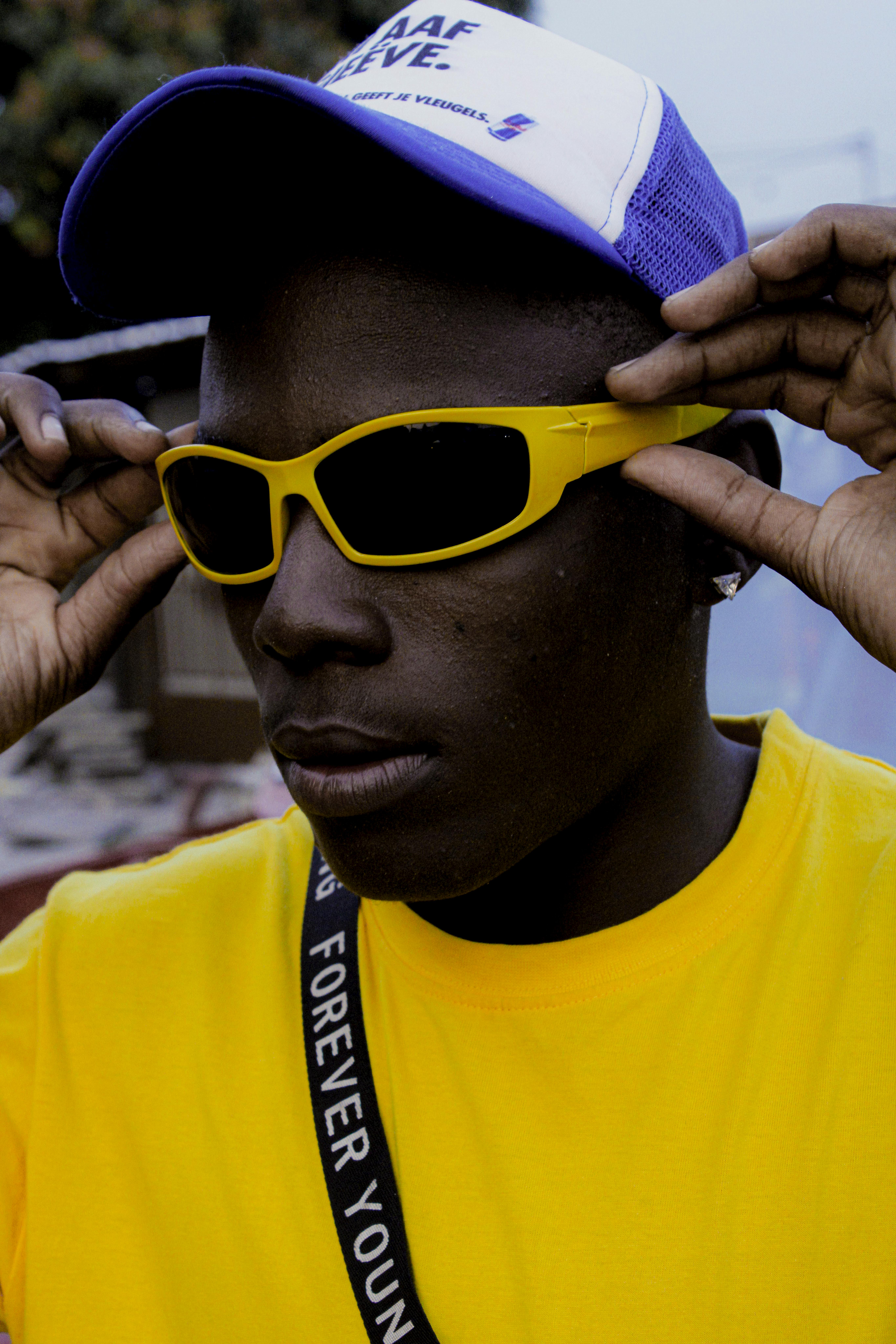 A fashionable man wearing yellow sunglasses and a cap, exuding a vibrant urban style.