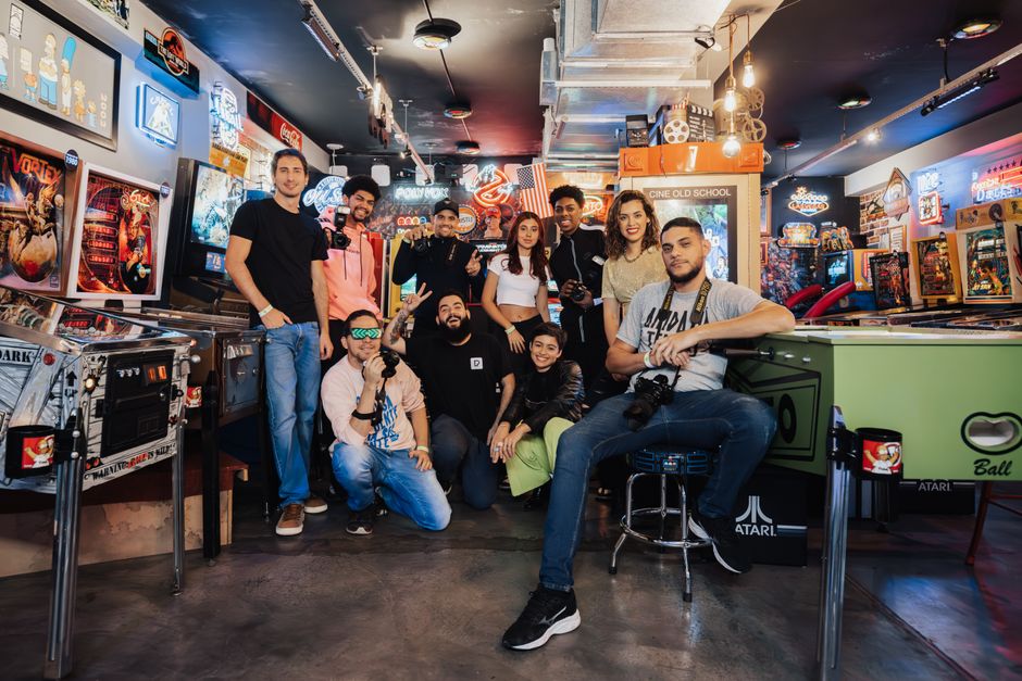 A lively group of friends gather in an arcade, surrounded by pinball machines and neon lights. A lively group of friends gather in an arcade, surrounded by pinball machines and neon lights.