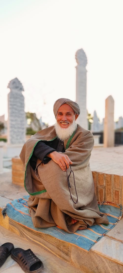 Smiling Man in Traditional Clothing Sitting at Cemetery