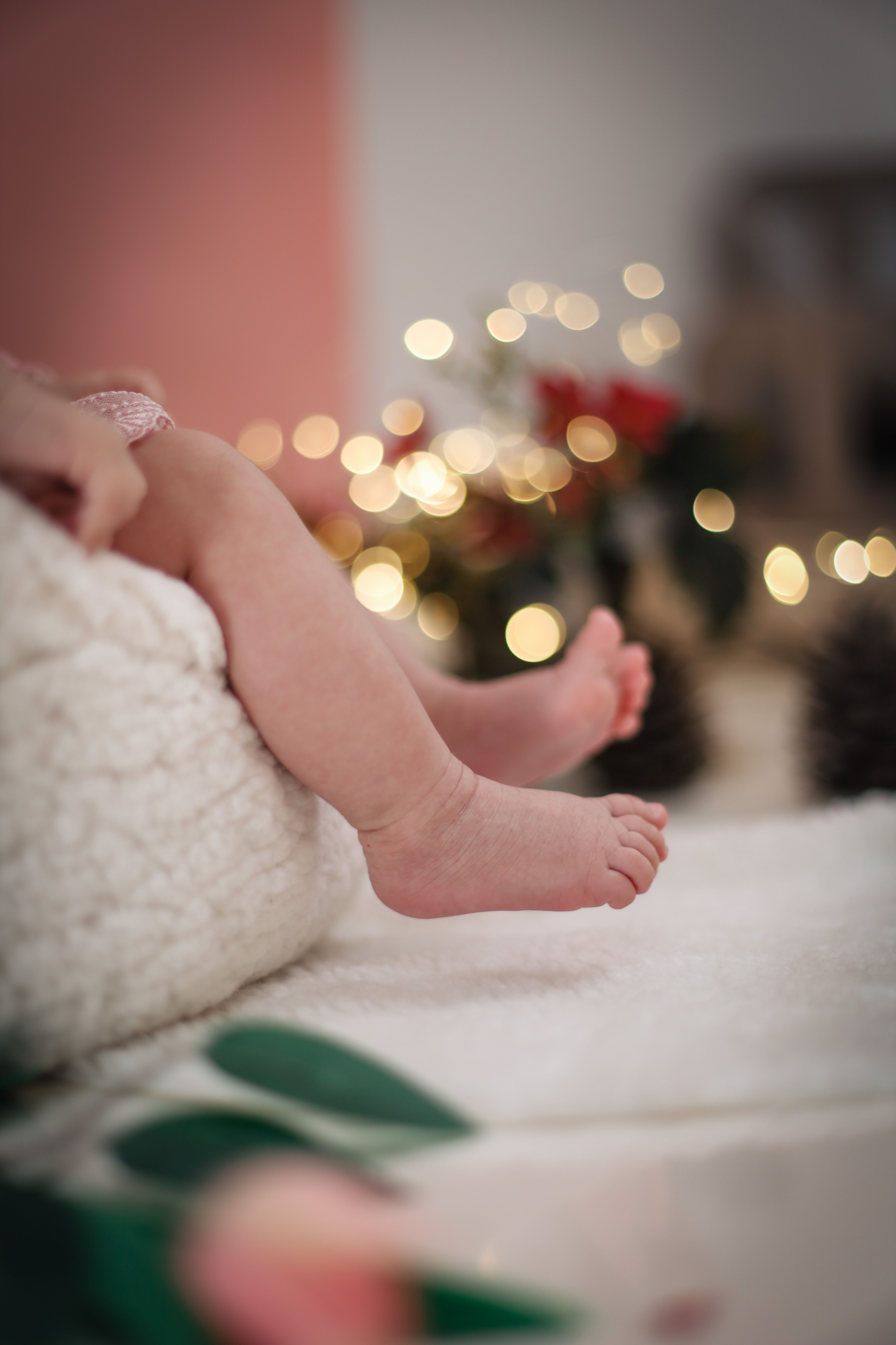 Close-up of a baby's feet surrounded by warm holiday lights, creating a cozy festive ambiance.