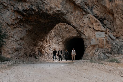 Group of men walking out of a rocky tunnel entrance in a rugged landscape.