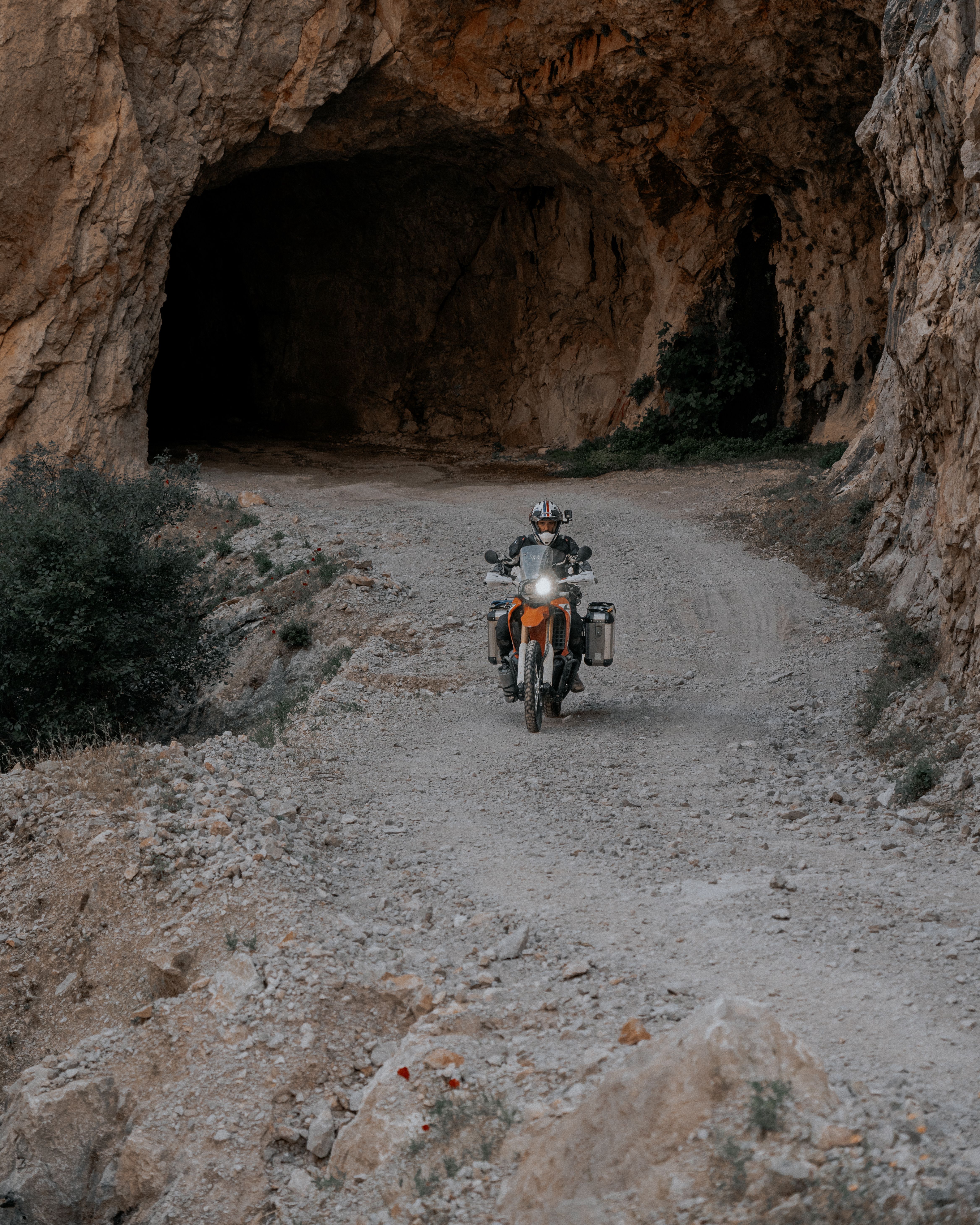 Motorcyclist on adventure tour riding through a rocky desert cave entrance.