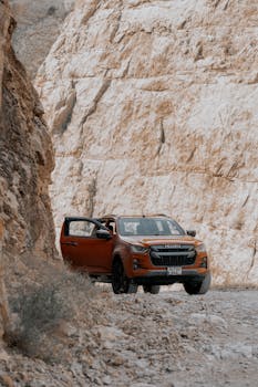 An orange SUV driving through rough, rocky terrain on a clear day.