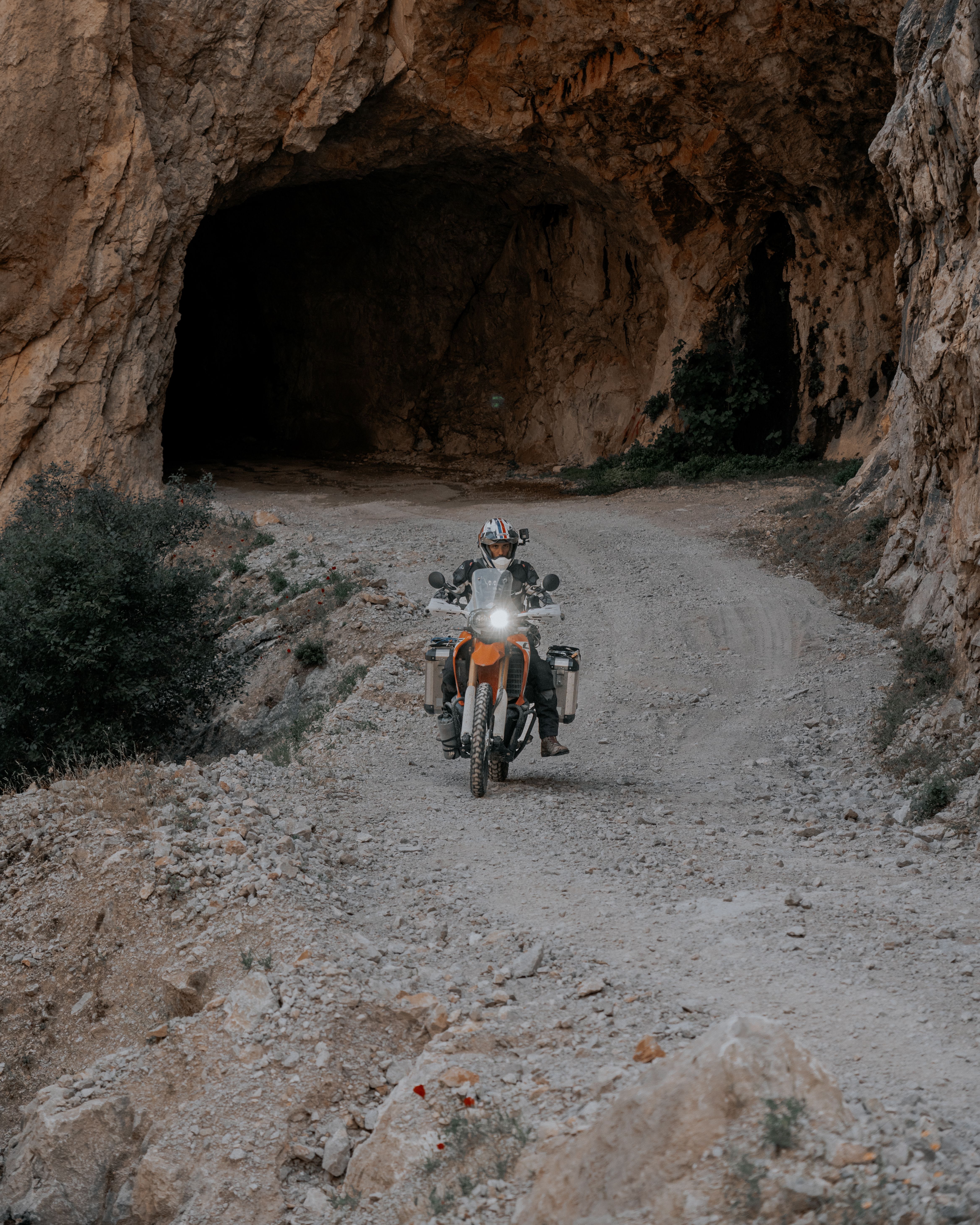 Motorcyclist ventures through a rugged cave entrance on a dirt road, capturing the thrill of exploration.
