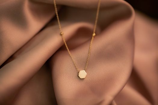 A delicate gold necklace resting on luxurious pink satin fabric.
