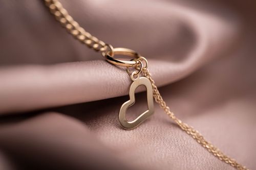 Free Close-up of a gold heart pendant necklace elegantly draped over soft, pink fabric with a delicate link chain. Stock Photo