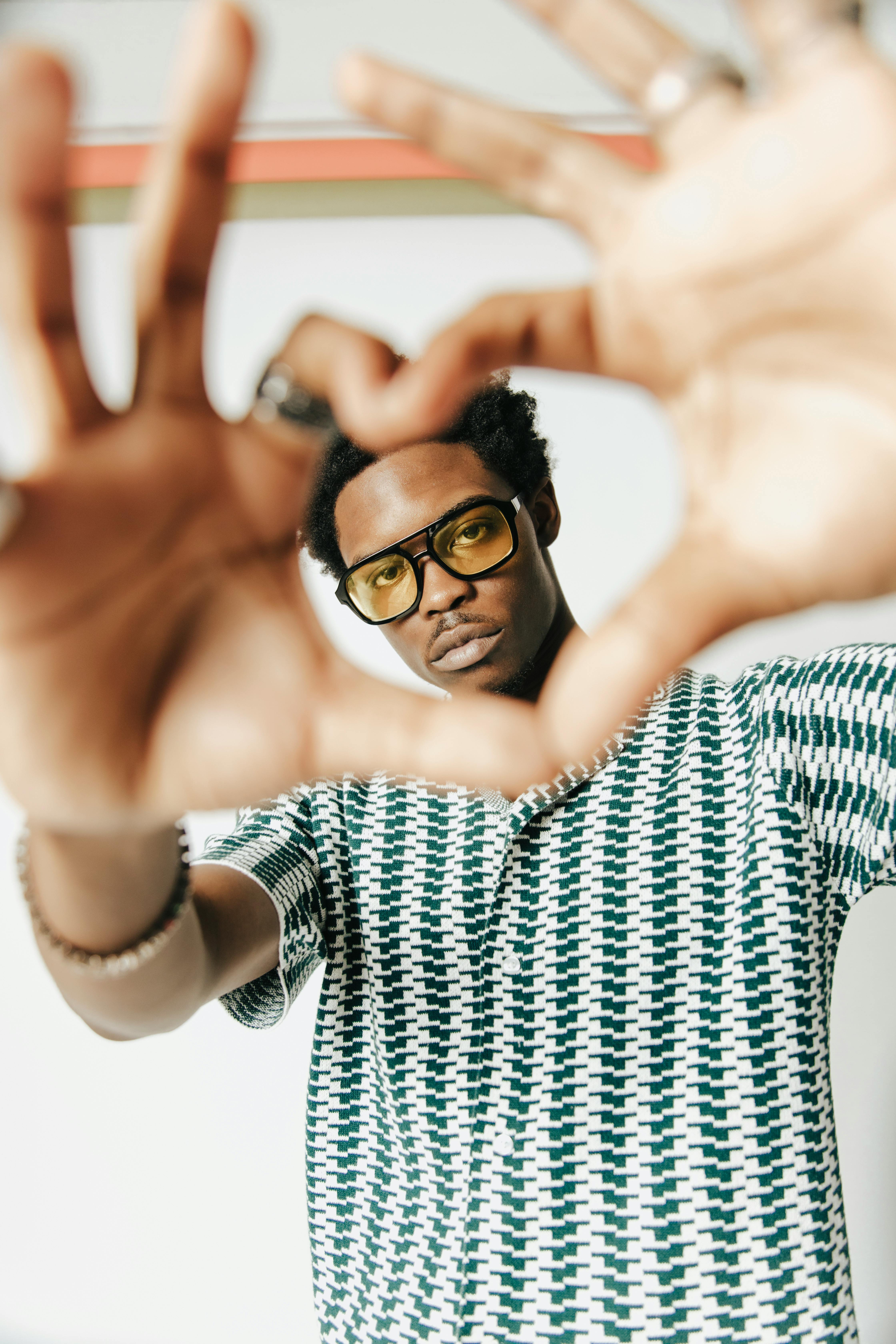 Young man wearing eyeglasses making a heart shape with hands in a portrait pose.