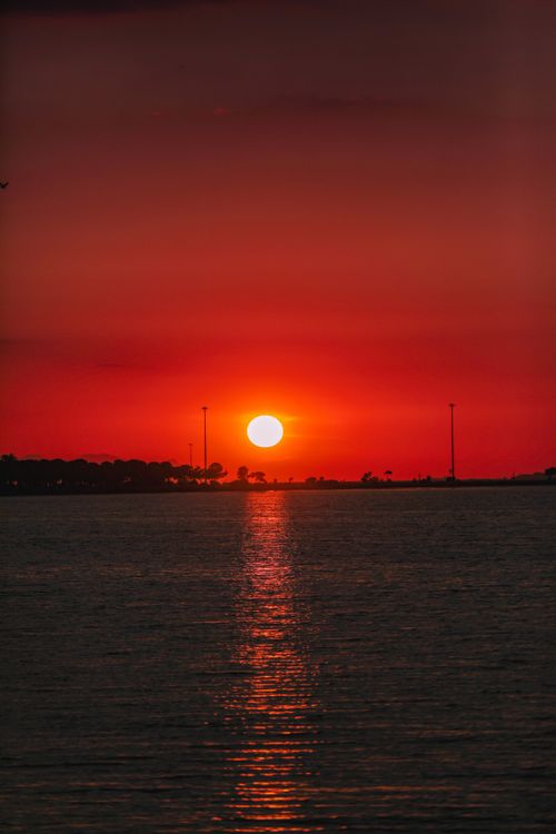 Free Stunning red sunset casting a reflective glow over tranquil water surface. Stock Photo