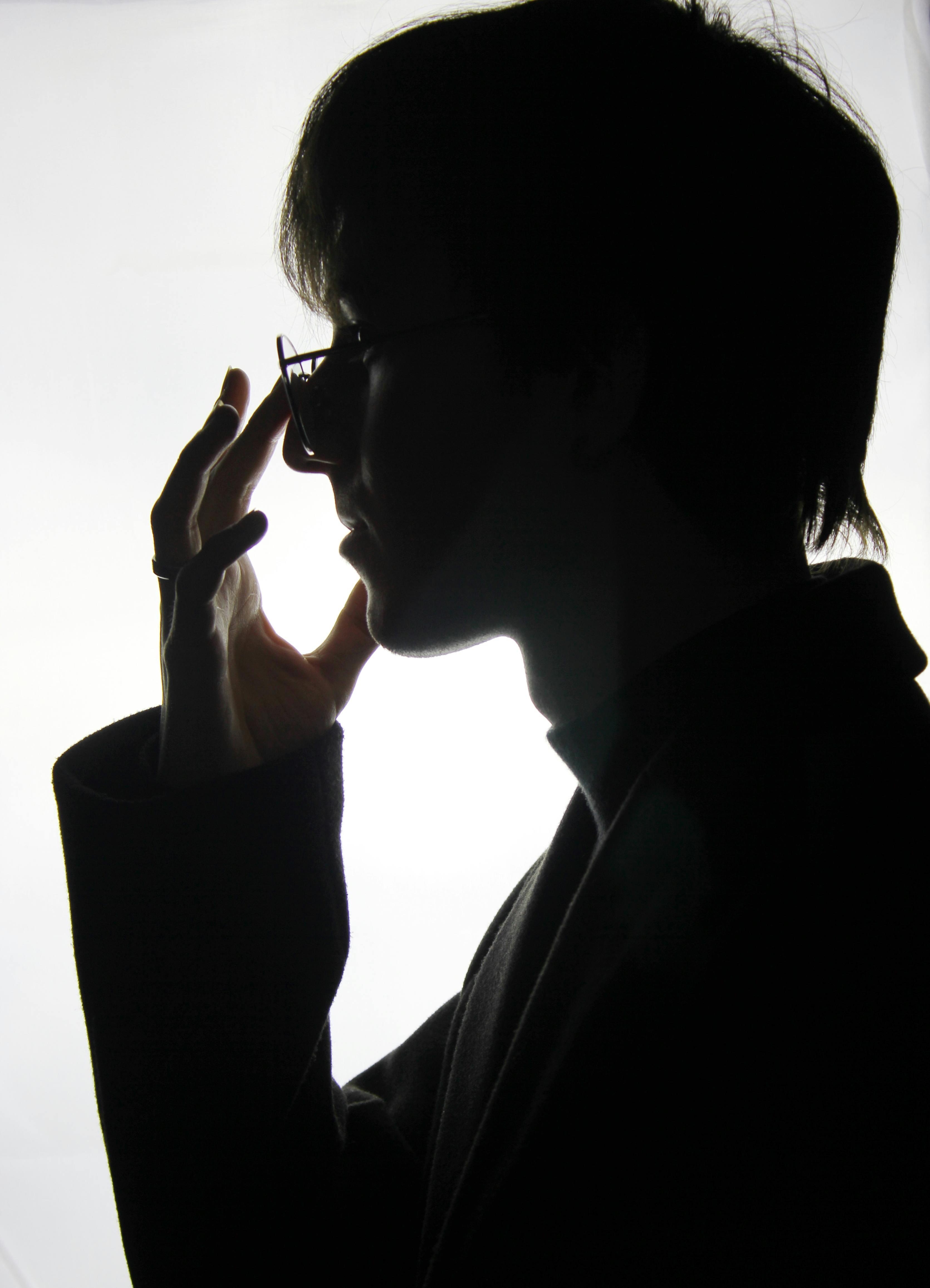 Artistic silhouette of person adjusting eyeglasses, creating a dramatic profile effect.