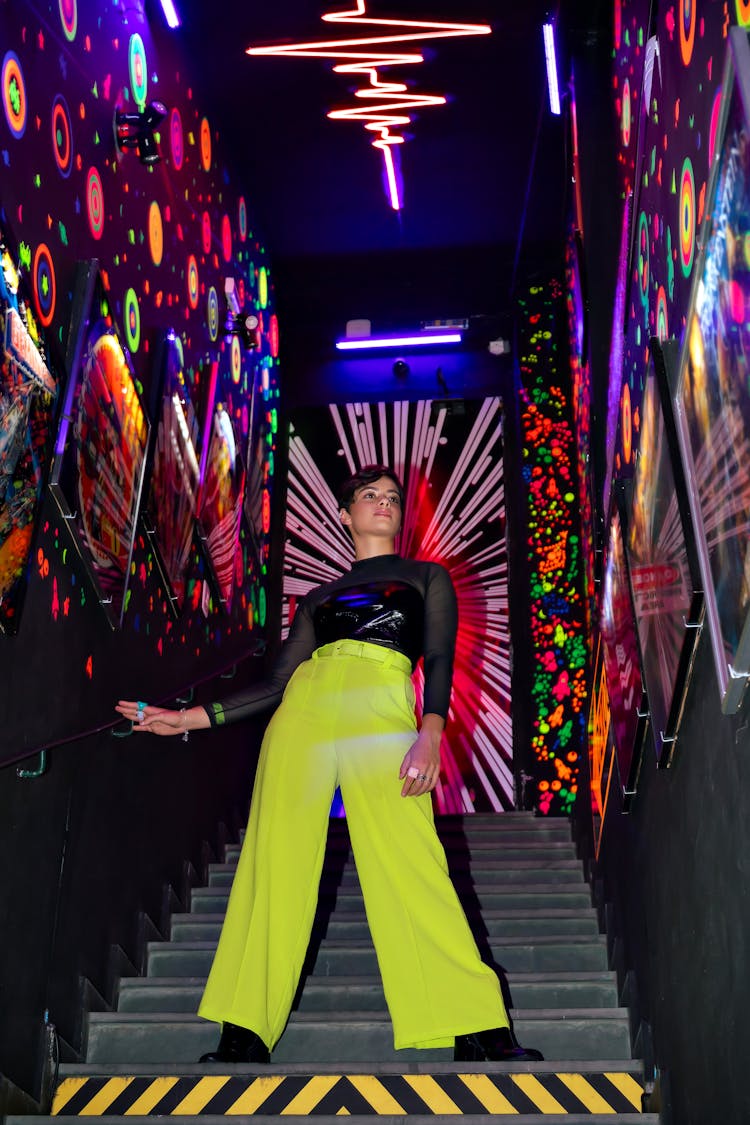 Woman In Green Pants And Black Blouse Posing On The Stairs Of A Night Club 