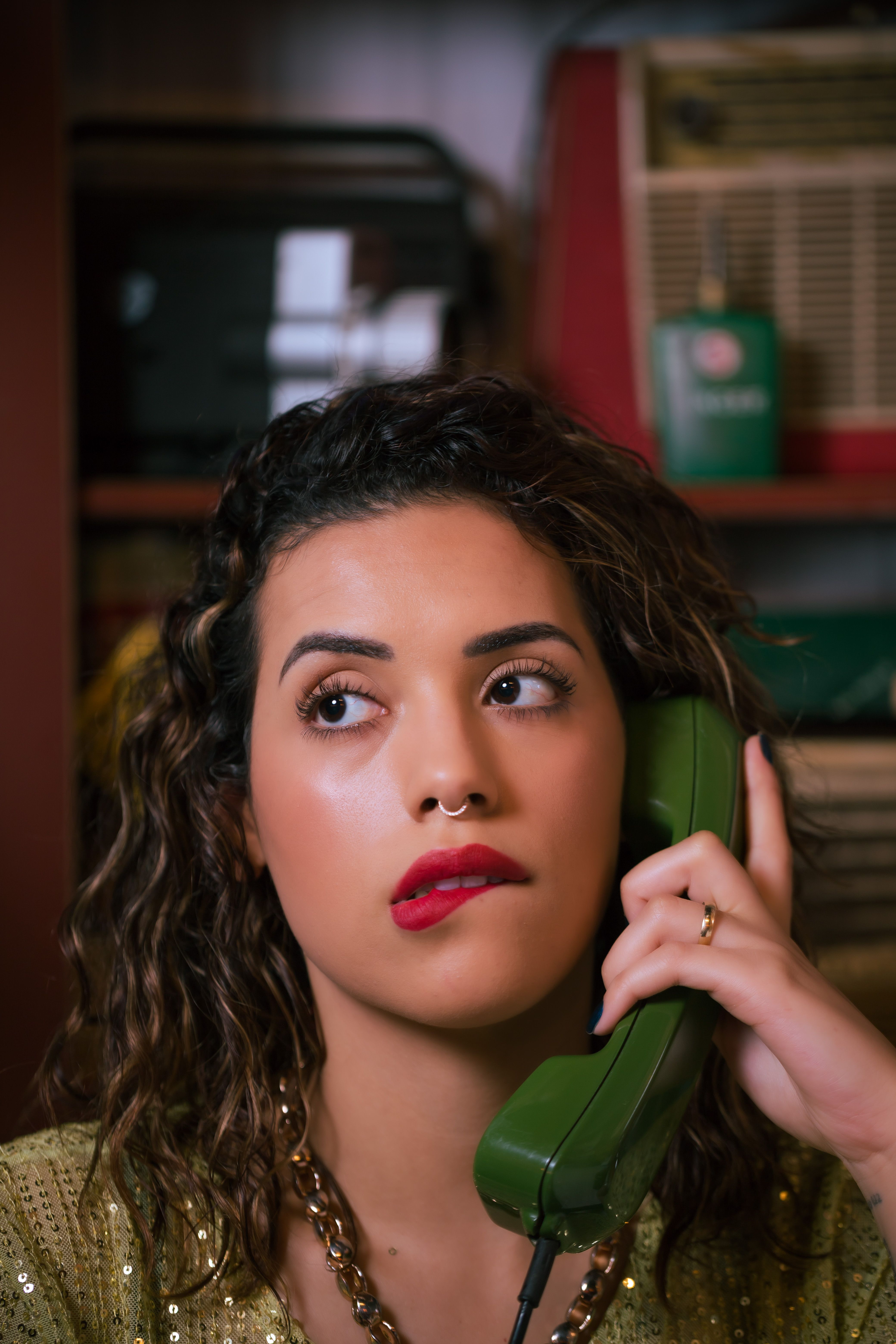 Woman with red lipstick holding a green vintage phone, reflecting a retro style.