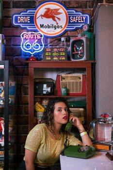 Portrait of a woman in a retro diner setting with vintage decor and telephone.
