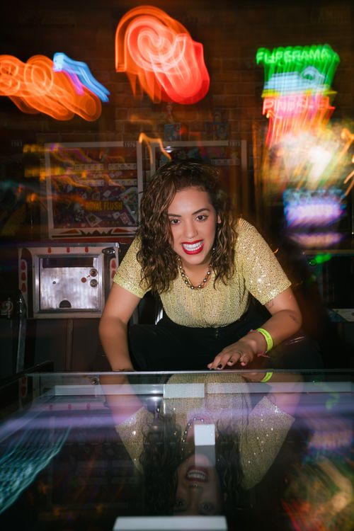 Free Woman playing pinball surrounded by colorful neon lights, creating an energetic vibe. Stock Photo