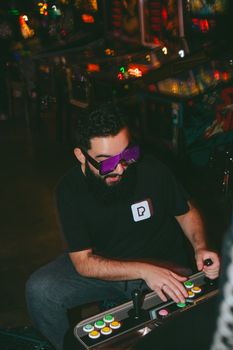 Adult man with beard enjoying arcade gaming in retro neon environment.