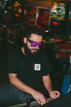 Bearded man enjoying a pinball game in a vibrant neon-lit arcade setting.