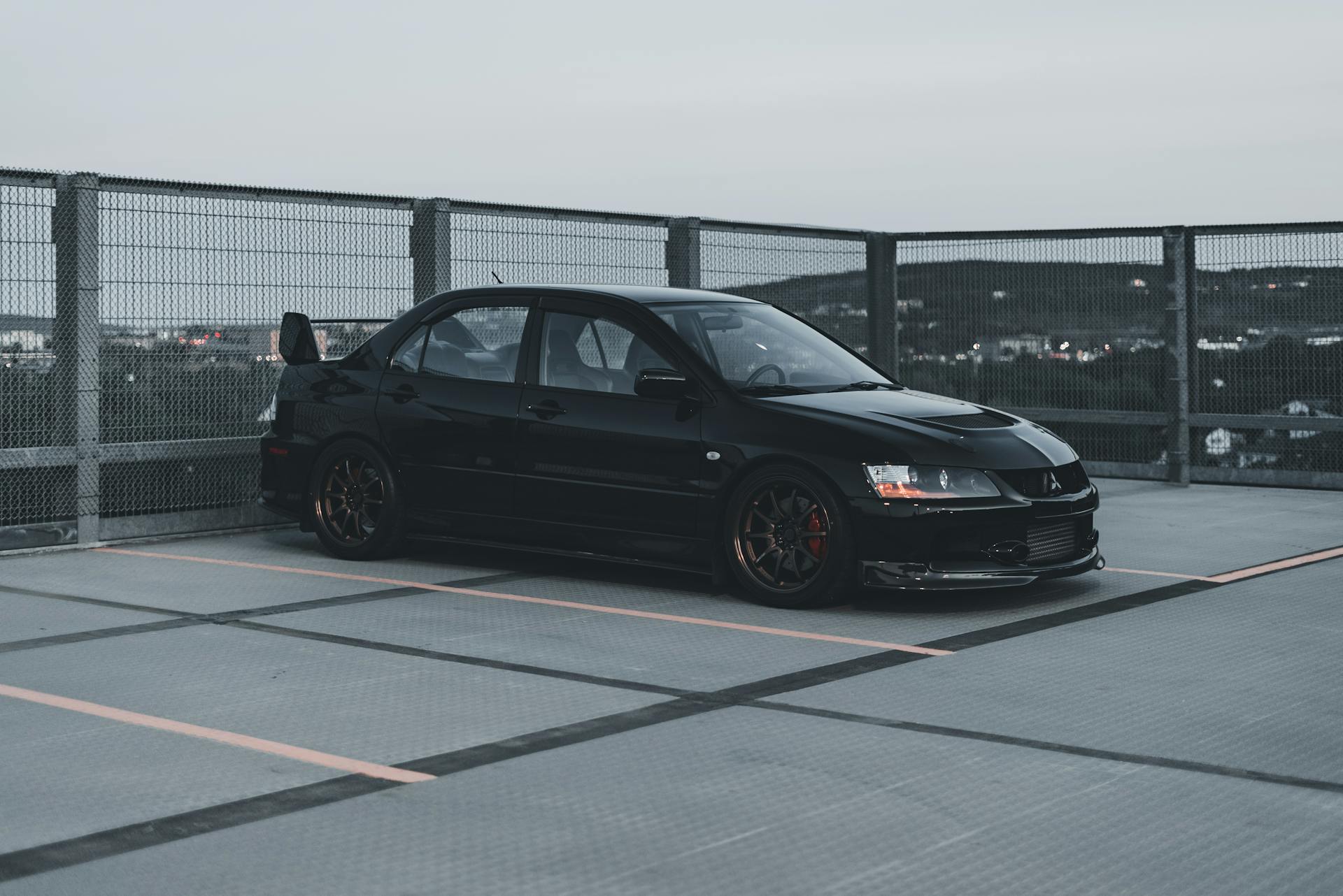 Stylish black Mitsubishi Lancer Evolution parked in an urban rooftop parking lot at dusk.