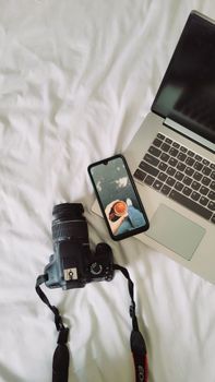 A laptop, camera, and smartphone arranged on a white bed, capturing the essence of modern technology and leisure.