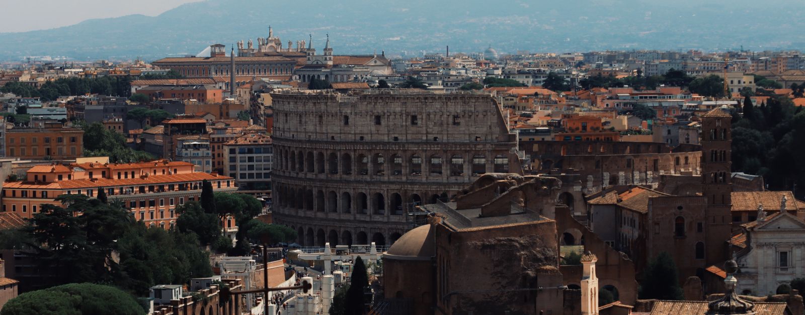 Drone shot of the iconic Colosseum and surrounding cityscape in Rome, Italy.