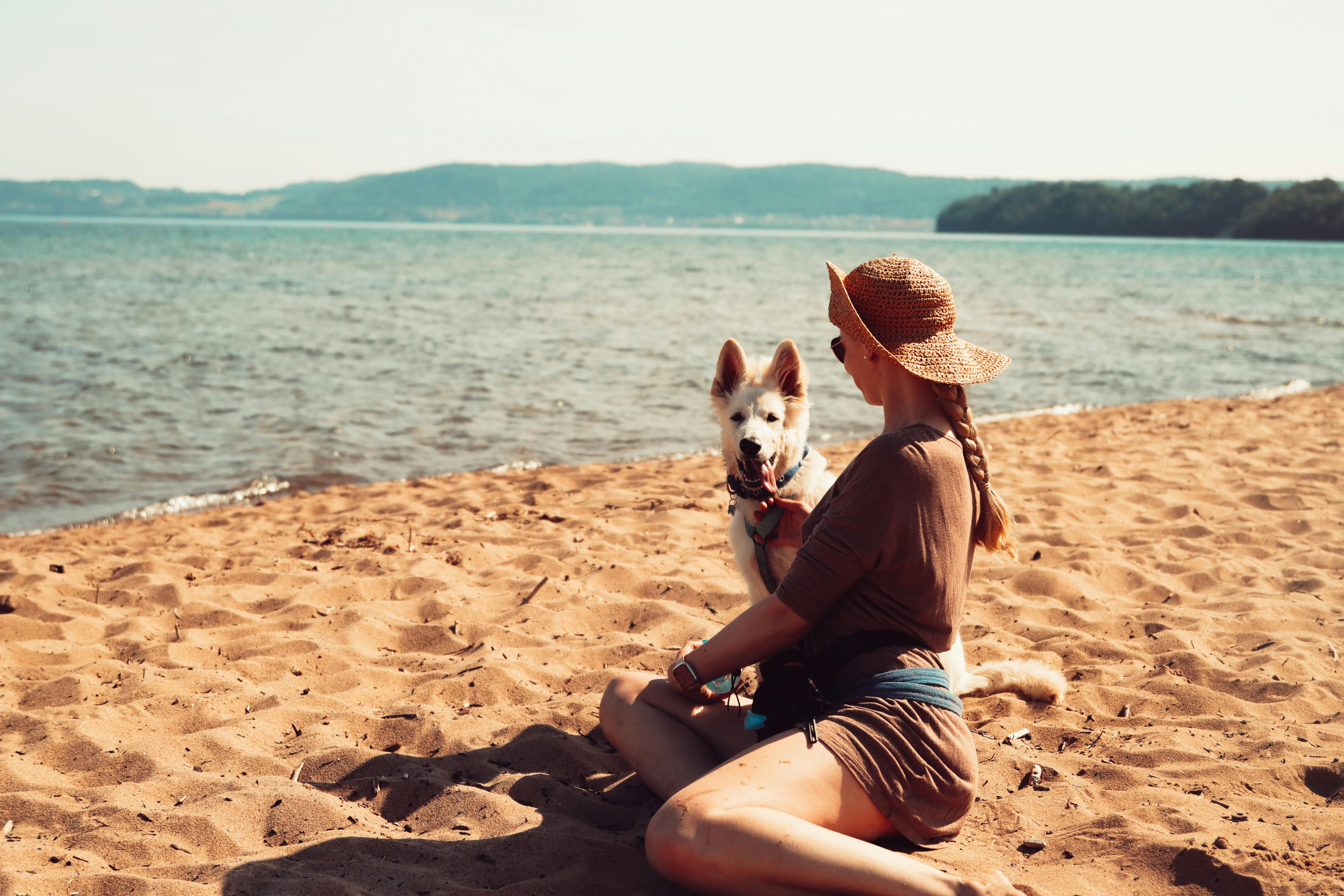 A woman sitting with her dog on the sandy beach of Lake Vättern in Jönköping, Sweden.