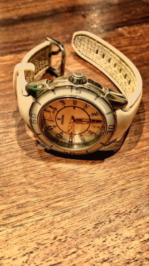 круглые серебристо белые аналоговые часы с белым резиновым ремешком на коричневой деревянной поверхности