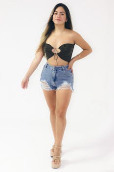 Fashionable young woman posing in denim shorts and top against a white studio background.