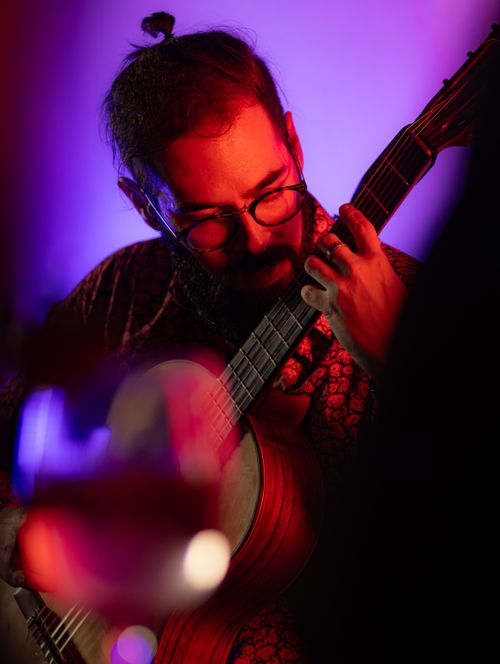 Free A bearded musician plays an acoustic guitar, set against moody purple lighting in an indoor setting. Stock Photo