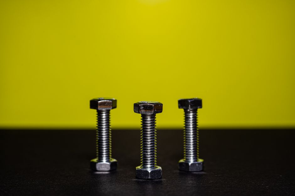 Close-up image of three steel bolts standing upright against a contrasting yellow background.