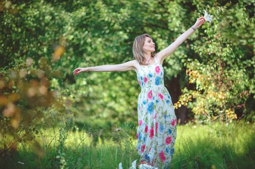Free A caucasian woman in a floral dress joyfully embraces nature in a sunny park. Stock Photo