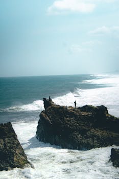 A scenic view of a person standing on a rocky cliff by the ocean, perfect for travel inspiration.