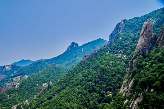 A scenic view of lush green mountains with rocky peaks under a clear blue sky.