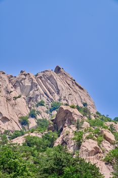 A scenic view of a sunlit rocky mountain with lush greenery against a clear blue sky.