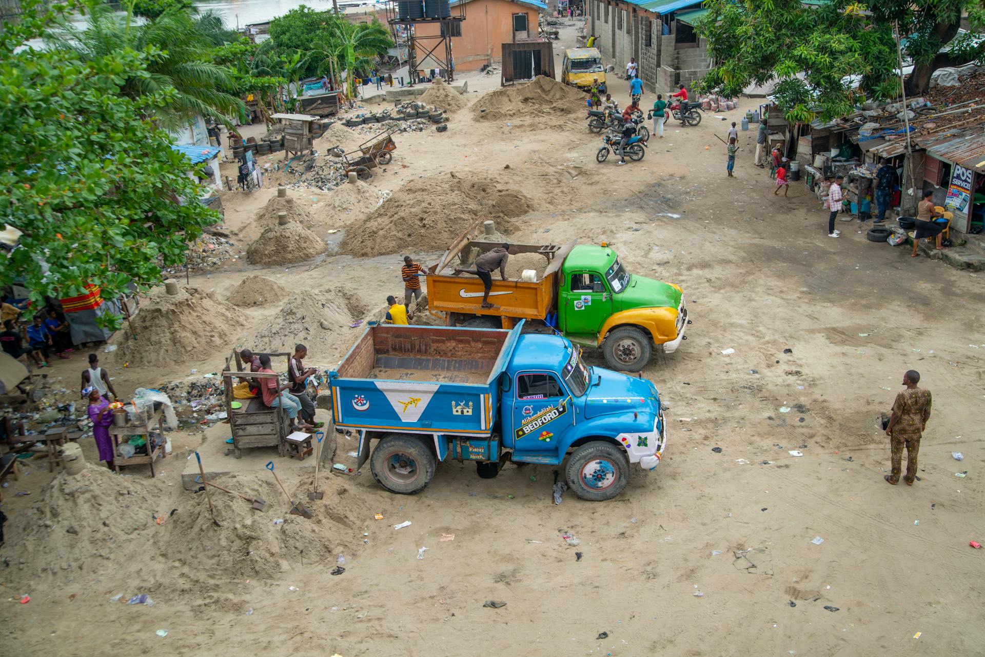 High-angle view of trucks and people in a rural Nigerian village, showcasing daily life.