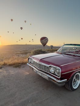 Vintage Chevrolet car at sunrise with hot air balloons in Göreme, Türkiye.
