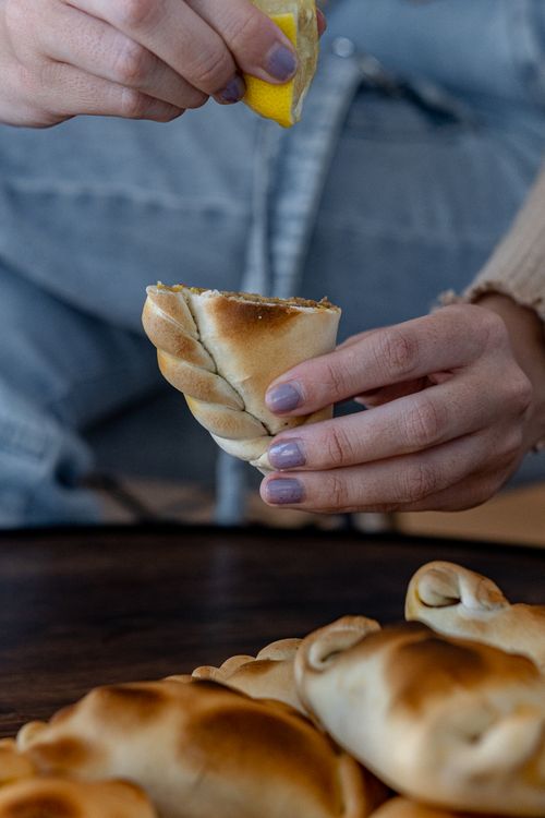 Free Woman squeezing lemon over freshly baked empanada indoors. High-quality culinary image capturing artisanal food preparation. Stock Photo