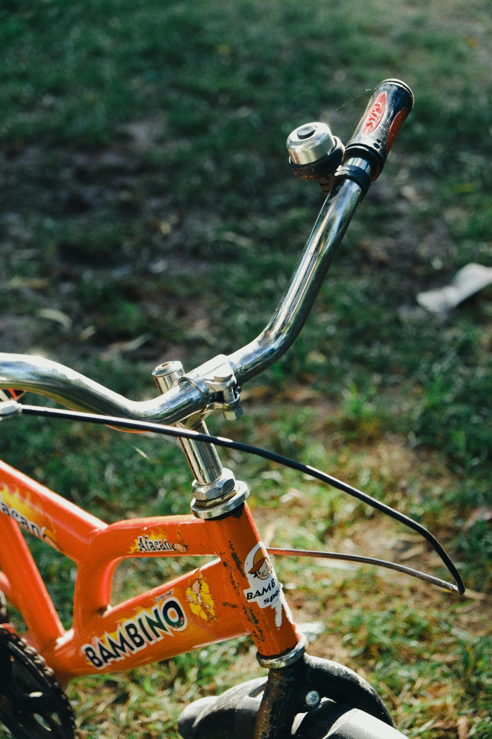 Detailed view of a red child's bicycle with handlebars and bell, on grass.