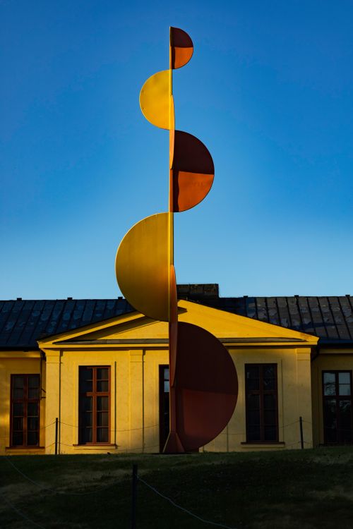 Free A contemporary sculpture in front of a historic yellow building during daylight. Stock Photo
